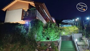 A modern house with a balcony, surrounded by lush greenery and a stone wall.