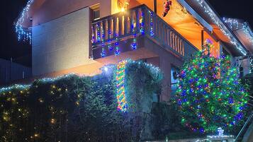 Una casa con balcón, rodeada de vegetación y luces navideñas.