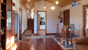A spacious living room with a wooden floor, a blue rug, a dining area with a table and chairs, and a staircase leading to an upper level.