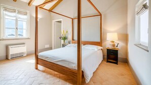 Un dormitorio con cama con dosel, una mesita de noche con lámpara, un radiador y una ventana con cortinas.