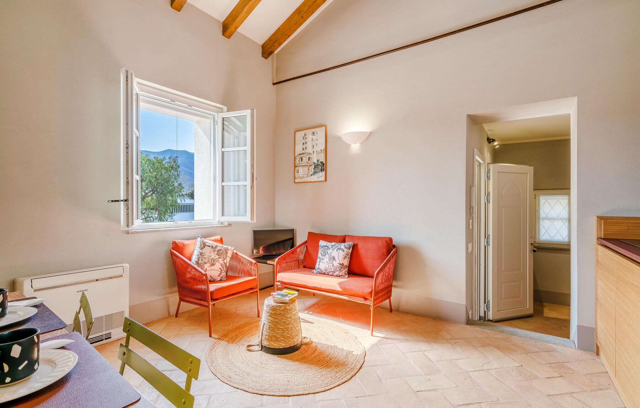 Una sala de estar acogedora con un sofá, una mesita y un televisor. Se aprecia una ventana con vistas al exterior, y una puerta que da a otra habitación.