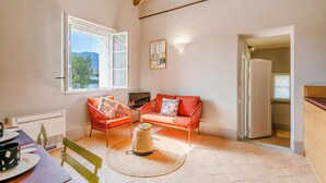 Una sala de estar acogedora con un sofá, una mesita y un televisor. Se aprecia una ventana con vistas al exterior, y una puerta que da a otra habitación.