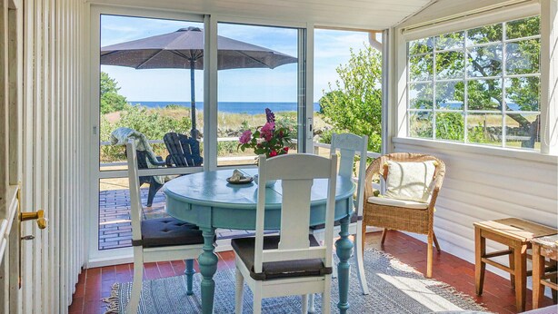 A sunroom with a table and chairs, large windows with a view of the ocean, and a wicker chair. - Gorgeous home in Svaneke with WiFi (Svaneke)