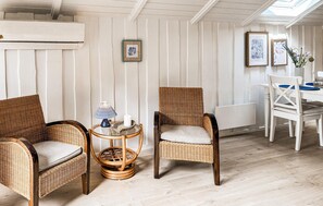 Ein Zimmer mit Korbstühlen, einem kleinen runden Tisch mit Kerze und gerahmten Pflanzenabbildungen an der Wand.