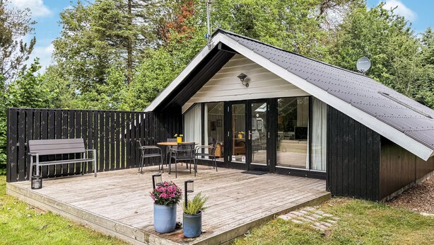 Une maison moderne avec un toit en pente, une terrasse dotée de mobilier d’extérieur et une grande porte-fenêtre coulissante.