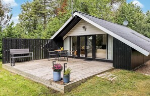 A modern house with a sloped roof, a deck with outdoor furniture, and a large sliding glass door.