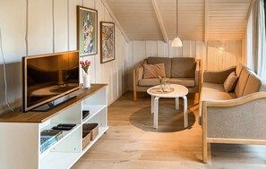 A cozy living room with a flat-screen TV, a sofa, a round coffee table, and a bookshelf.