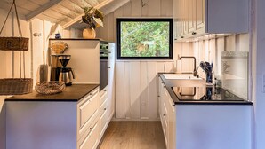 Une cuisine avec des meubles en bois, une machine à café et une fenêtre donnant sur un paysage verdoyant.