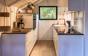 Een keuken met houten kastjes, een koffiezetapparaat en een raam met uitzicht op groen.