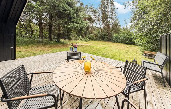 A wooden deck with a round table and chairs, surrounded by a grassy area and trees.