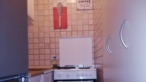 Une cuisine compacte avec une cuisinière, un four et un lave-vaisselle blancs. Deux poignées sont fixées au mur sur le côté droit, et un panneau rouge est placé au-dessus de la cuisinière.