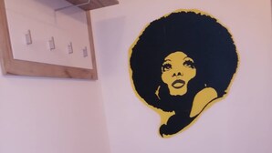 Une pièce comprenant un meuble blanc à deux tiroirs et un plateau noir, un mur orné d’une œuvre d’art circulaire, et une étagère en bois avec un luminaire.