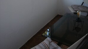Une petite pièce avec une fenêtre donnant sur un espace vert, une table en verre avec une lampe et un coussin à rayures.