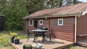 En stuga av trä med en veranda, ett bord med stolar och krukväxter.