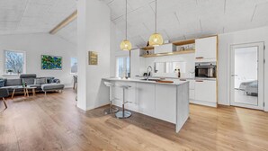 Une cuisine moderne avec des meubles blancs, un îlot central et des luminaires suspendus.