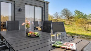 Un espace de restauration en plein air avec une table dressée pour deux personnes, un vase rempli de fleurs et une assiette de fruits.