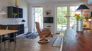 A modern living room with a leather recliner, a dining area with a wooden table and chairs, a TV mounted on the wall, and a large window with a view of greenery. - Nice apartment in Allinge with WiFi (Allinge)