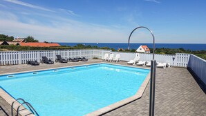 A rectangular swimming pool with clear blue water, surrounded by a white fence. There are several lounge chairs and a metal pool ladder. - Nice apartment in Allinge with WiFi (Allinge)