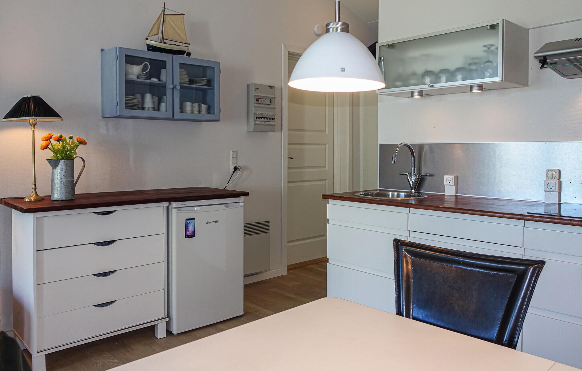 A compact kitchen with a refrigerator, a sink, and a cabinet with dishes.