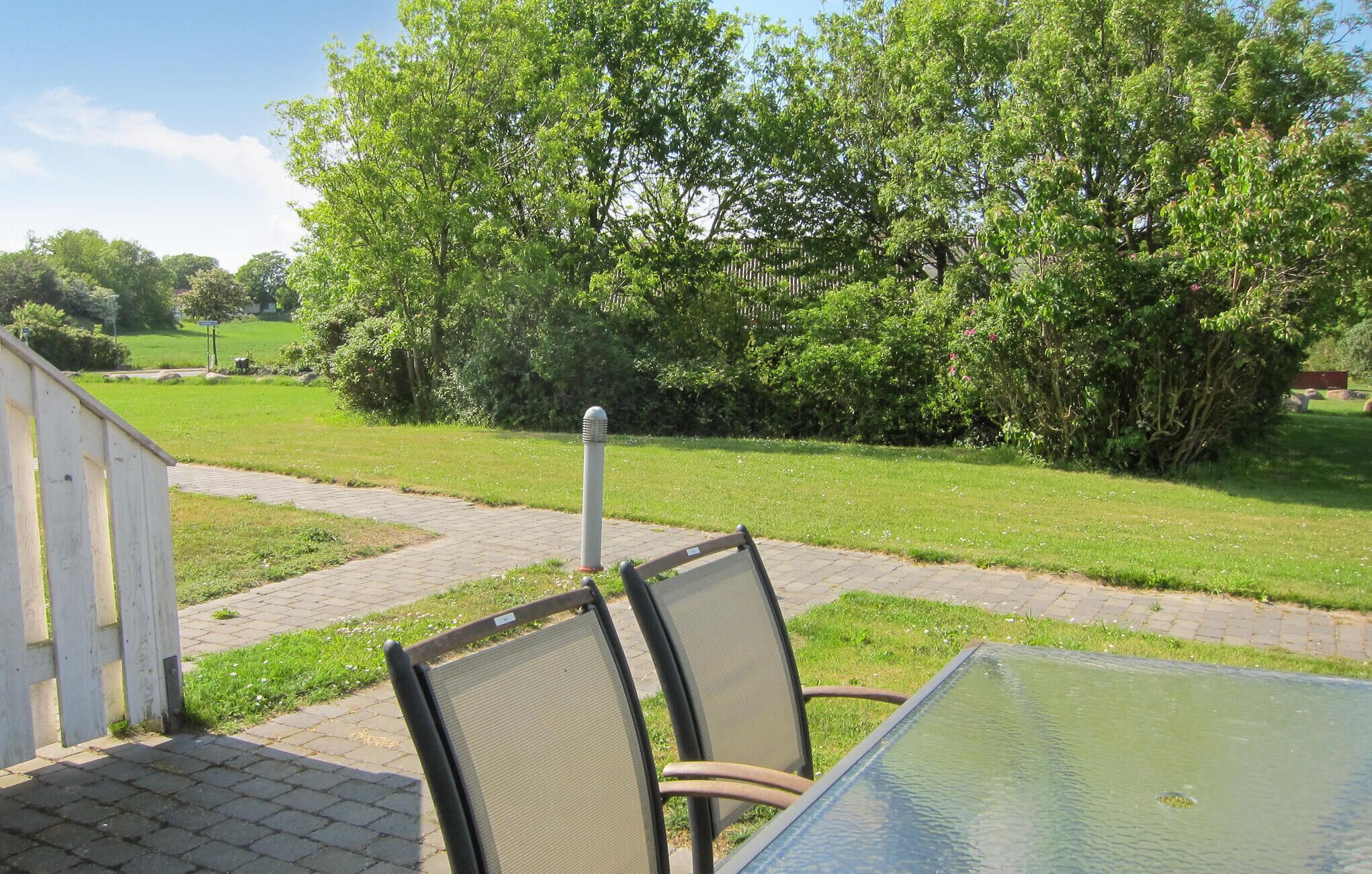 Une terrasse avec une table et des chaises, une clôture en bois et une zone herbeuse avec des arbres.