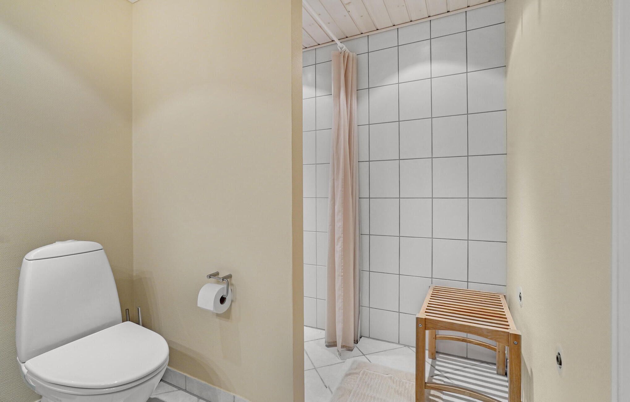 A bathroom with a toilet, a shower curtain, and a wooden stool.