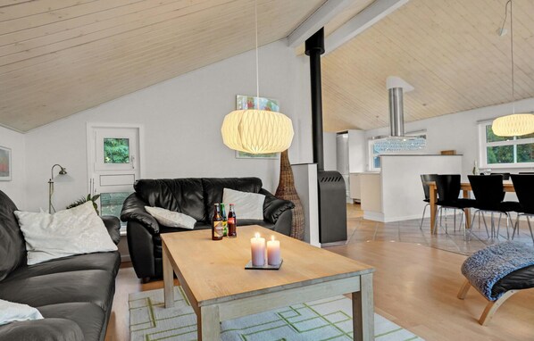 Una sala de estar moderna con un sofá de cuero negro, una mesa de centro de madera con velas, y un comedor con una mesa y sillas negras.