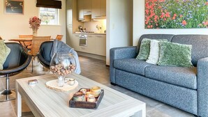 A modern living room with a grey sofa, a coffee table with candles, and a dining area with wicker chairs. - Awesome home in Diksmuide with WiFi (Diksmuide)
