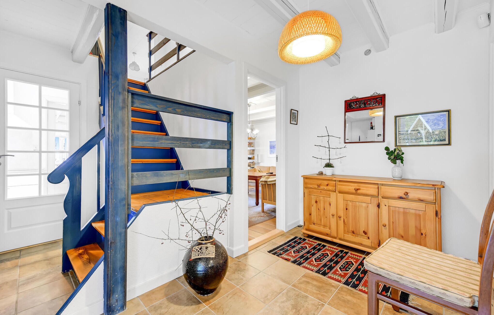A staircase with blue and orange steps, a wooden cabinet, a vase with branches, and a patterned rug.