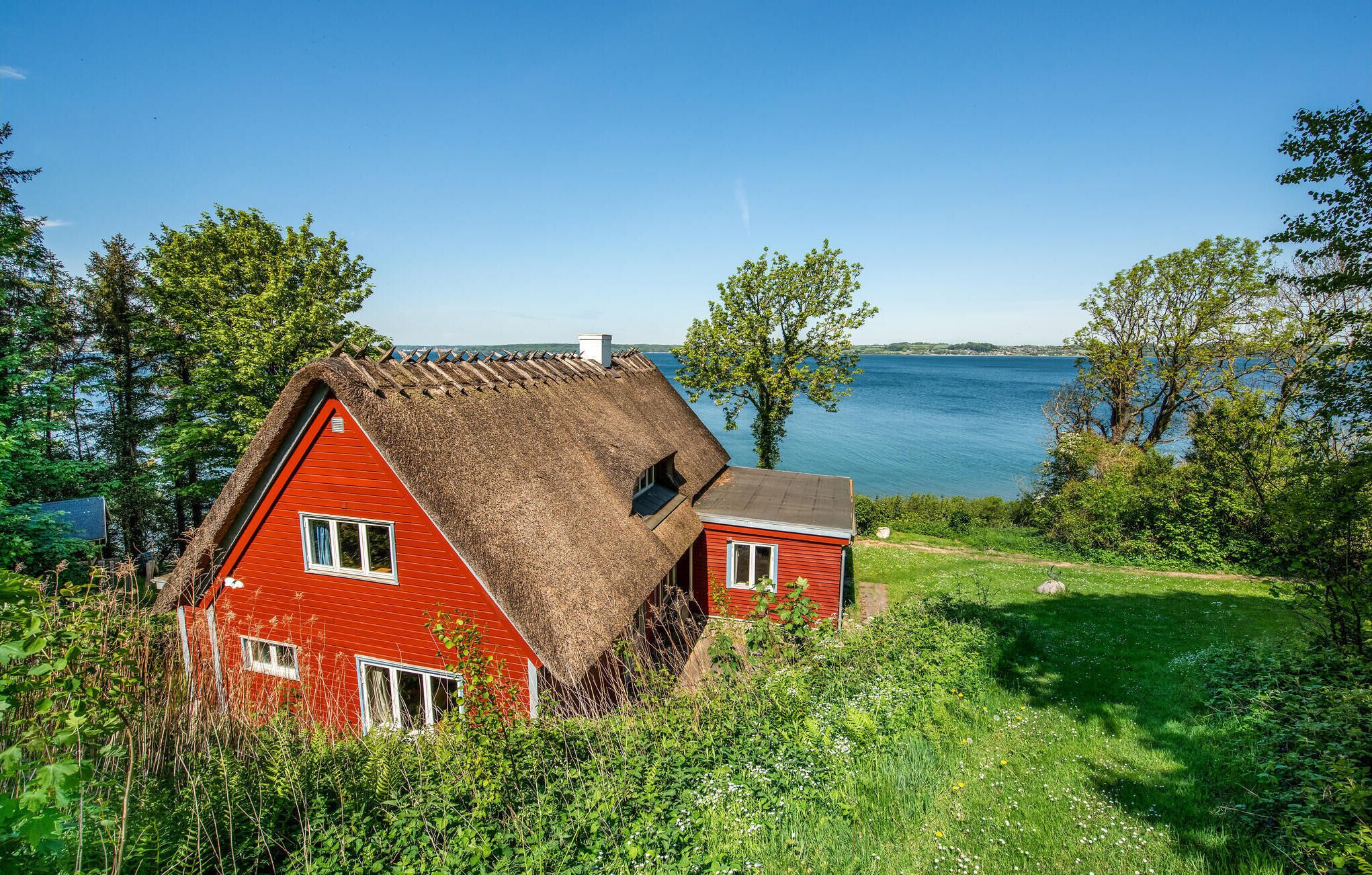Een rood huis met rieten dak, omgeven door groen en met uitzicht op een waterpartij.