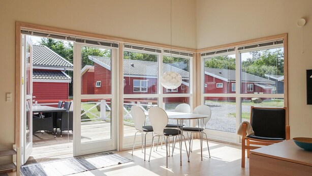 A room with large windows, a wooden floor, a white table, and a red building outside. - Gorgeous home in Gudhjem with WiFi (Gudhjem)