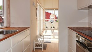 A narrow kitchen with wooden countertops, a built-in oven, and a view of a red house through a window. - Gorgeous home in Gudhjem with WiFi (Gudhjem)