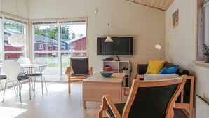 A modern living room with a dining area, a flat-screen TV, and a large window overlooking a red house. - Gorgeous home in Gudhjem with WiFi (Gudhjem)