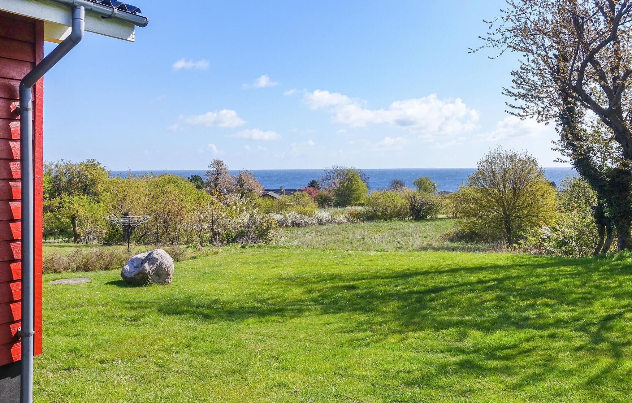 A grassy outdoor area with a view of the sea, a red building, and trees.