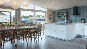 Una cocina moderna con una isla central, armarios blancos y una zona de comedor con sillas de mimbre.