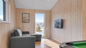 Ett modernt rum med träpanel på väggarna, en grå soffa, en tv och ett biljardbord.