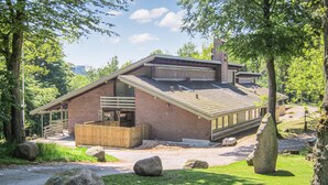 Een modern gebouw van baksteen met een schuin dak, grote ramen en een houten terras.