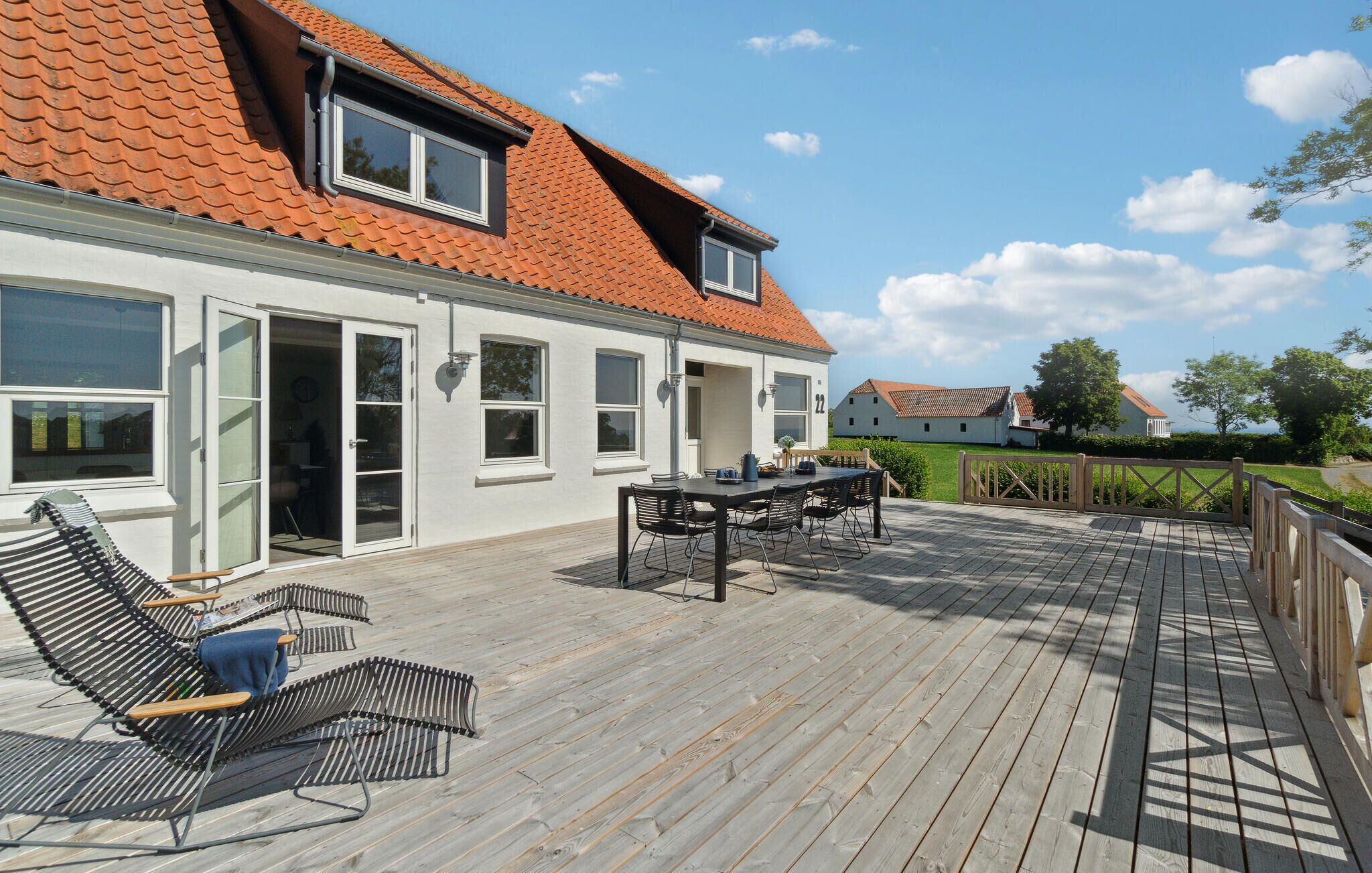 A house with a wooden deck, a dining area with chairs and a table, and a large window.
