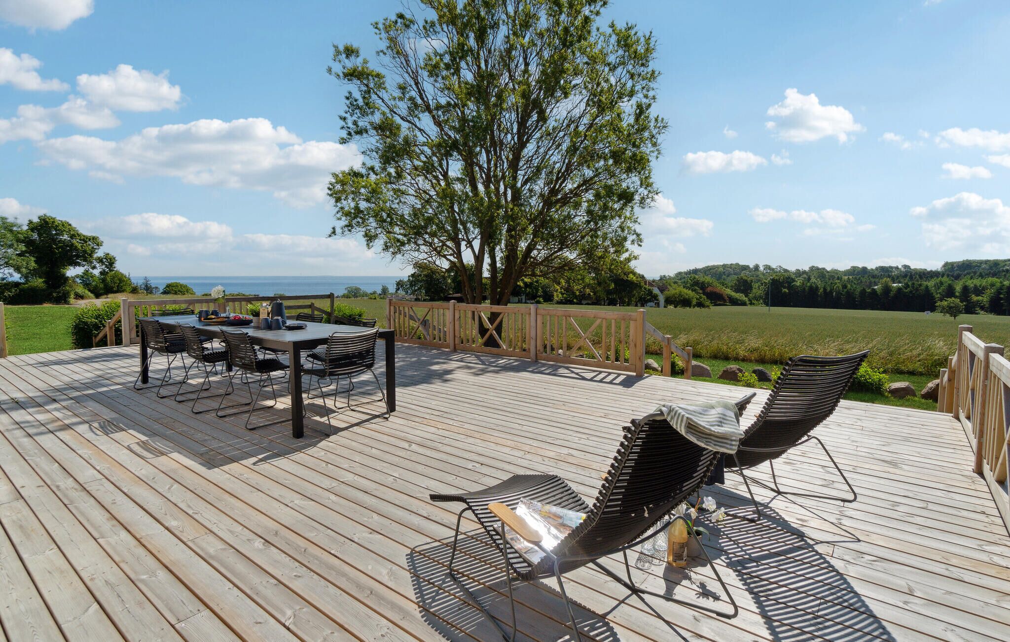 Een houten terras met een tafel, stoelen en een lounge stoel, met uitzicht op het landschap.