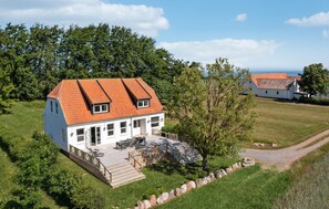 Ein weißes Haus mit rotem Dach, eine Terrasse mit Gartenmöbeln und ein Steinweg, der zum Eingang führt.