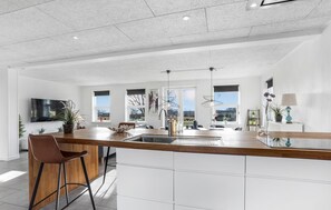 Une cuisine moderne dotée d’un îlot central, de meubles blancs et d’une grande fenêtre offrant une vue sur l’extérieur.