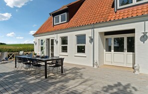 Un bâtiment blanc surmonté d’un toit recouvert de tuiles rouges, une terrasse avec des meubles d’extérieur et une vue panoramique sur la campagne.