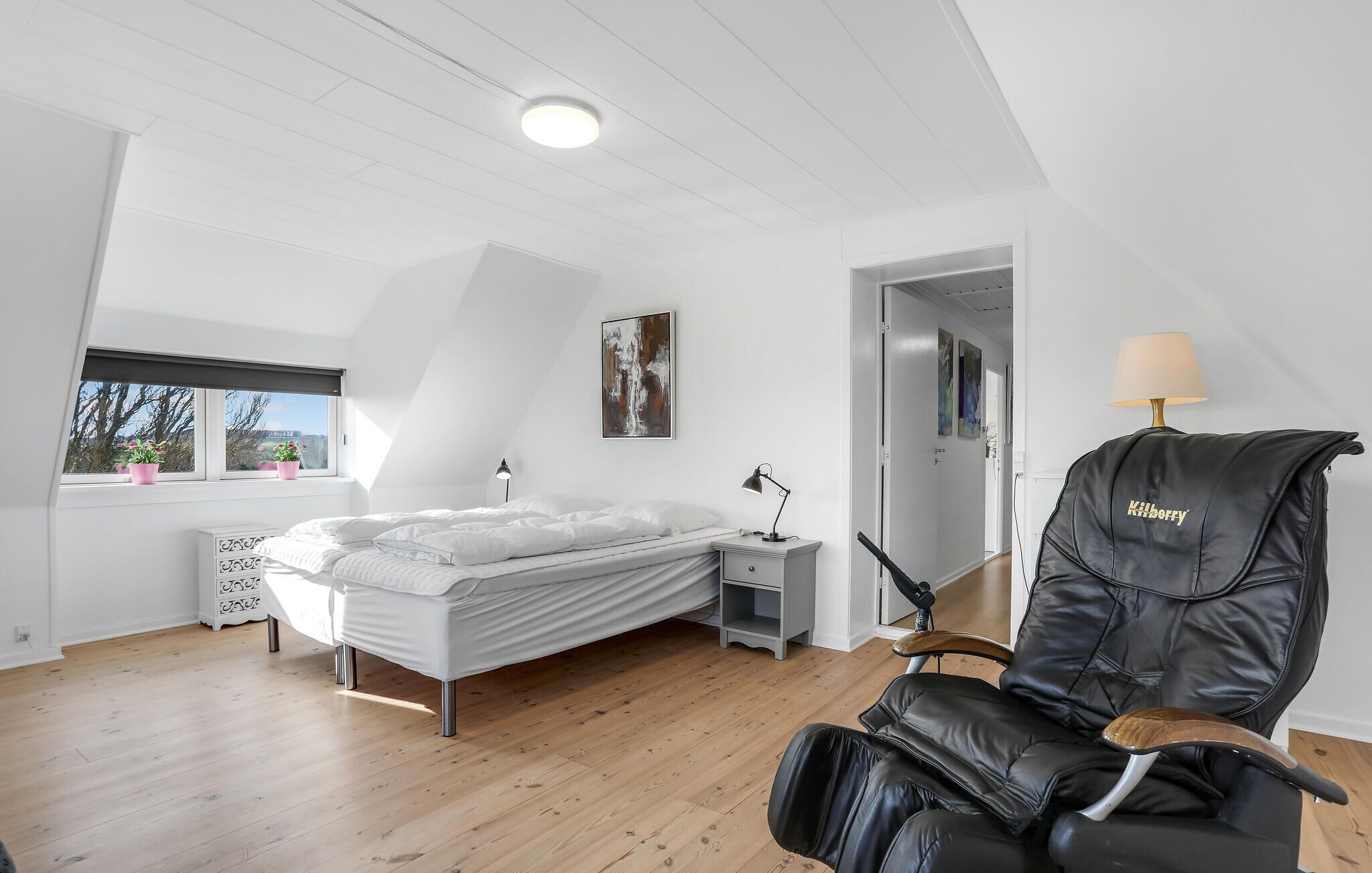 Een slaapkamer met een bed, nachtkastje, lamp en een stoel.