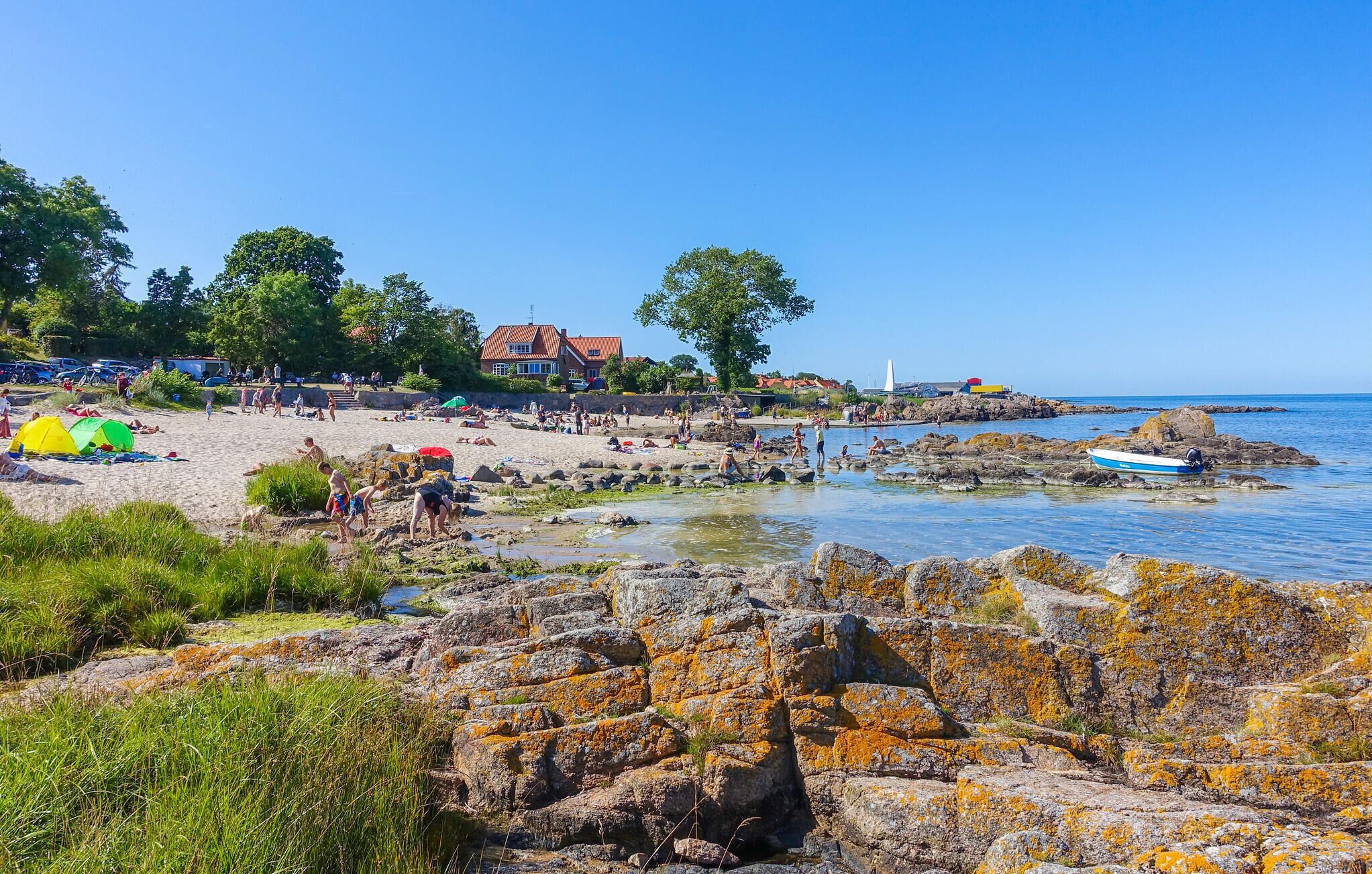 A beach with tents, rocky shoreline, and a clear blue sky.