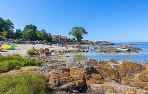 Ein Strand mit Zelten, felsigem Ufer und blauem Himmel.
