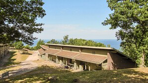 Un bâtiment rustique, doté d’un toit en pente, entouré d’arbres et offrant une vue dégagée sur l’océan.