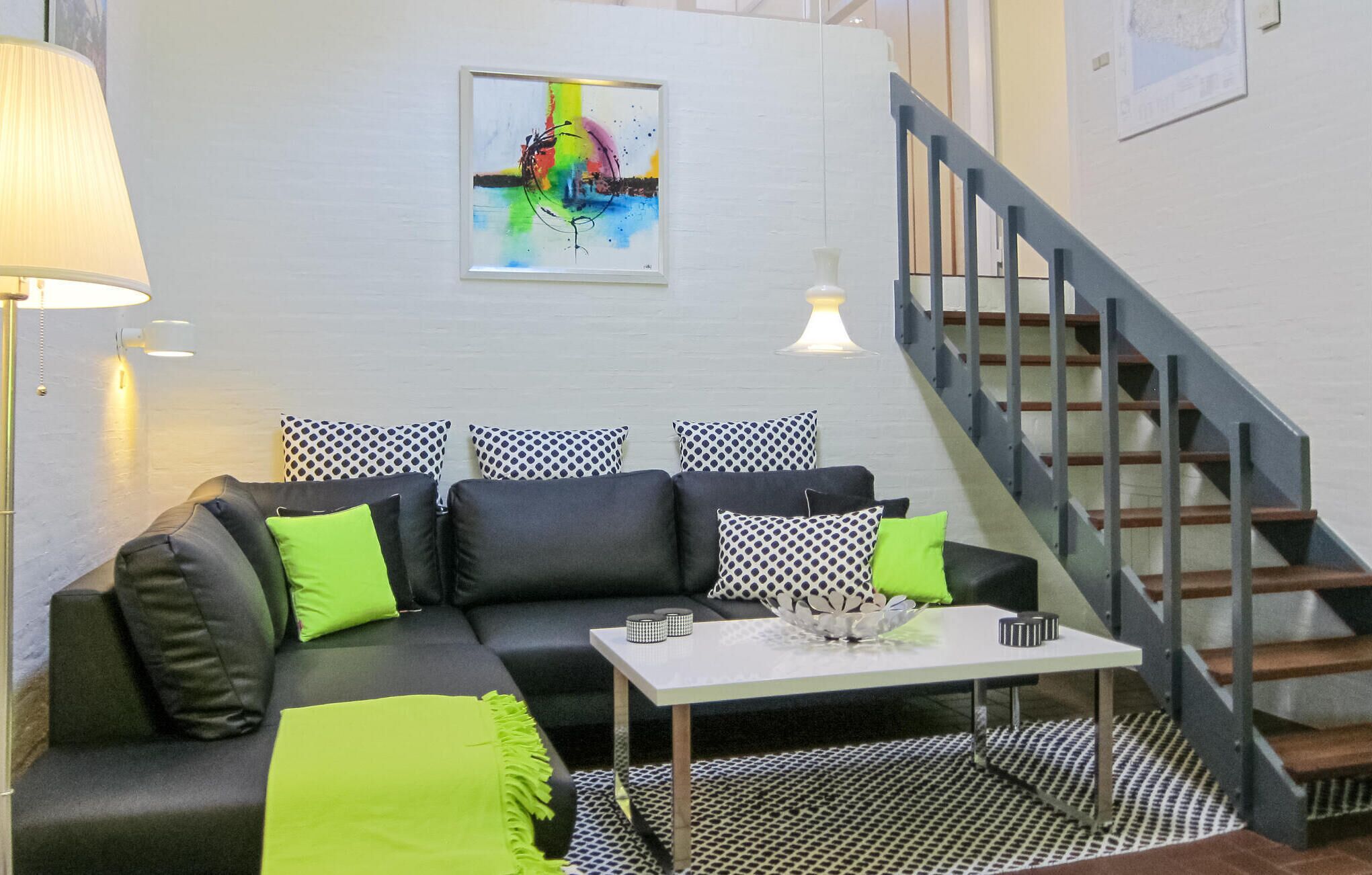 Un salon moderne avec un canapé à motifs noir et blanc, une table basse blanche et un escalier situé sur le côté droit.