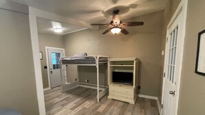 Una habitación con literas, ventilador de techo, televisor sobre un mueble y puerta con ventanal.