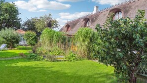 A traditional stone house with a thatched roof, surrounded by a well-maintained garden with various plants and a small pond. - Nice home in Nexø with WiFi (Nexø)