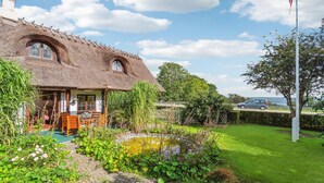 A thatched-roof house with a garden, a pond, and a flagpole. - Nice home in Nexø with WiFi (Nexø)