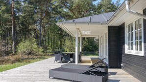 A covered outdoor area with a table and chairs, a wicker lounge chair, and a wooden deck. - 3 bedroom gorgeous home in Nexø (Nexø)
